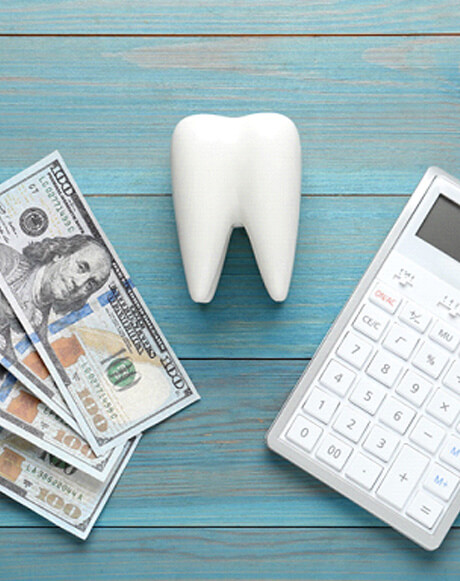 hundred dollar bills, a model tooth, and a calculator on a wooden blue surface