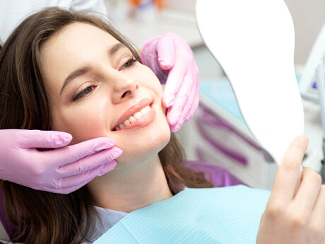 woman with brown hair smiling at her reflection in dental chair with dentist behind her
