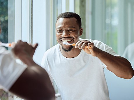 Man smiling while brushing his teeth in bathroom