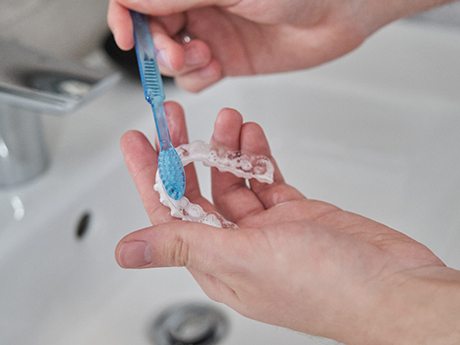 Patient using toothbrush to clean aligner