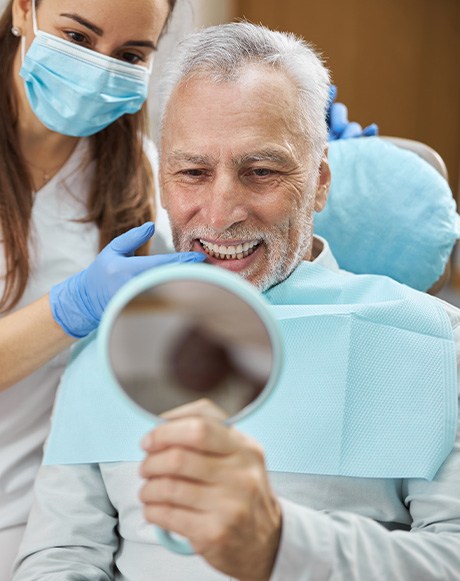 An older man admiring his new dental implants in a hand mirror