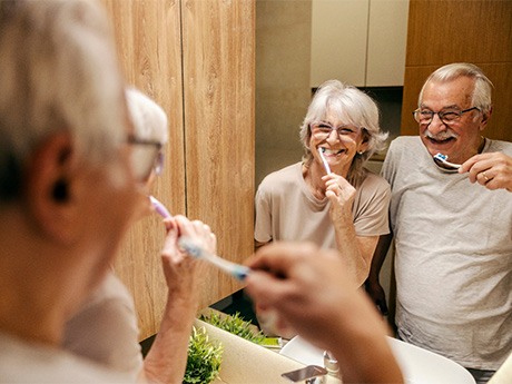 A happy older couple brushing their teeth in front of a bathroom mirror