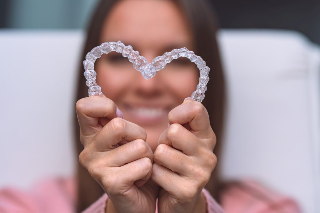 Woman in pink shirt holding Invisalign in a heart shape